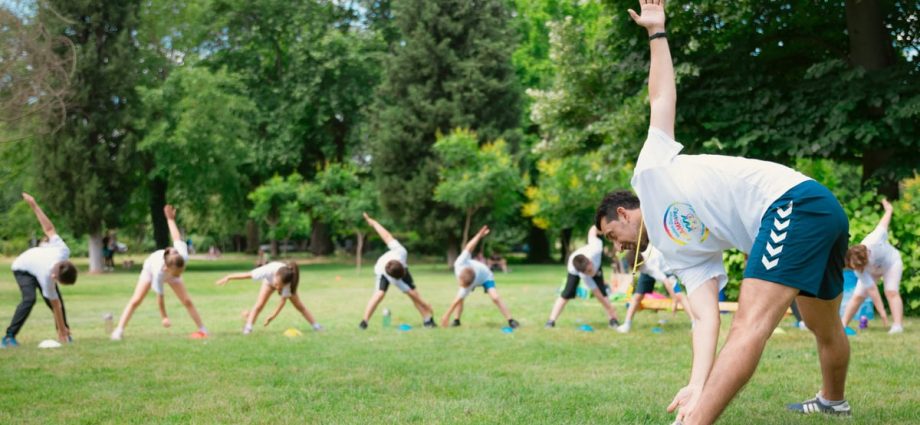 Kids stretching exercises in a park guided by a coach, promoting fitness and fun.