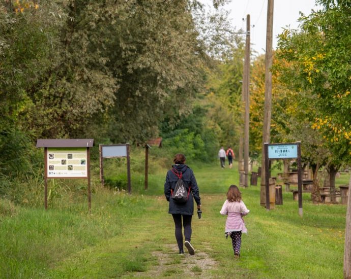 A parent and child walking on a path in a scenic nature reserve in Croatia, surrounded by lush greenery.