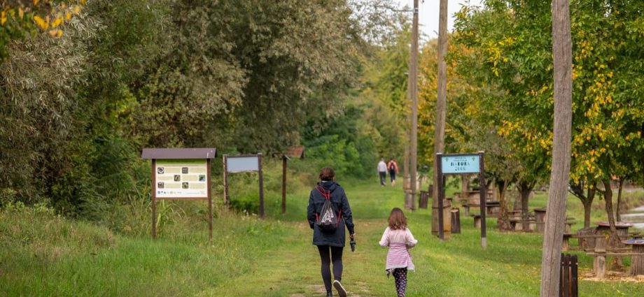 A parent and child walking on a path in a scenic nature reserve in Croatia, surrounded by lush greenery.