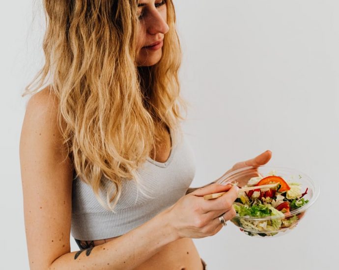 A caucasian woman in a sports bra enjoying a fresh salad, embodying healthy eating and lifestyle.