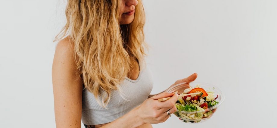 A caucasian woman in a sports bra enjoying a fresh salad, embodying healthy eating and lifestyle.